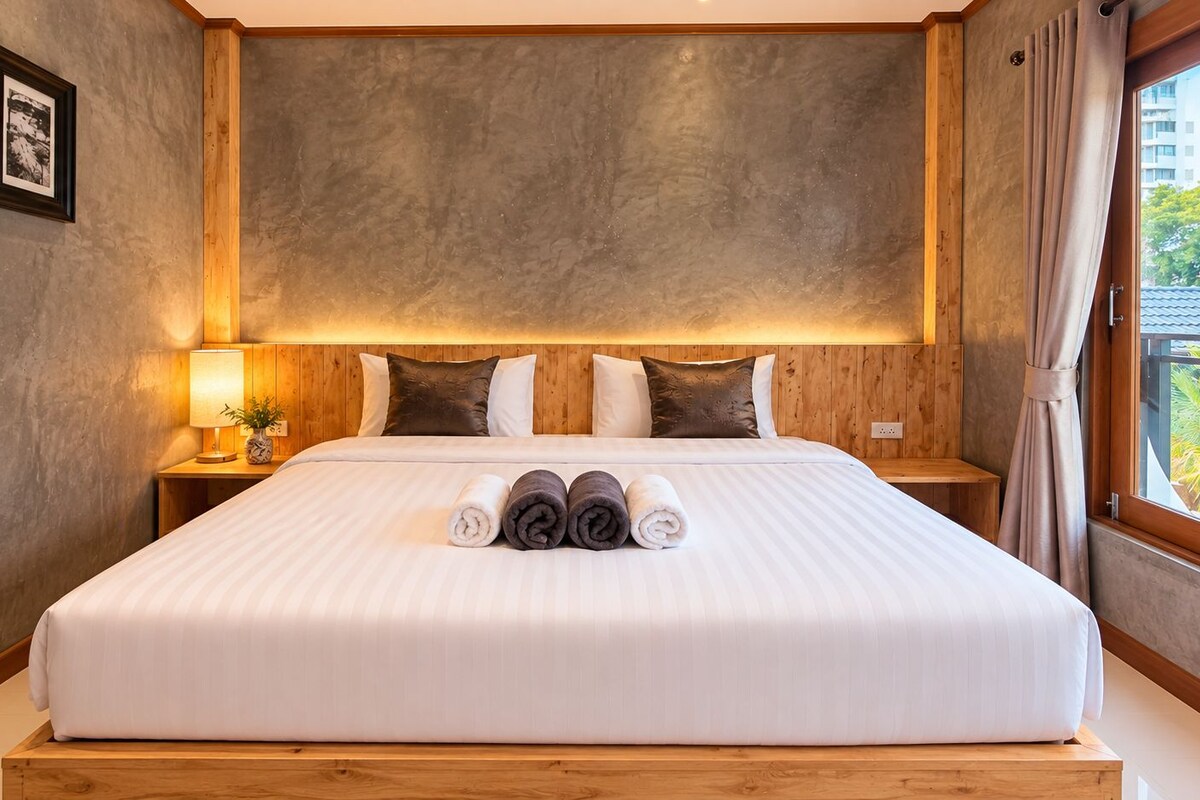 A hotel room with a large bed, wooden headboard, and a view of greenery outside.
