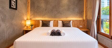 A hotel room with a large bed, wooden headboard, and a view of greenery outside.
