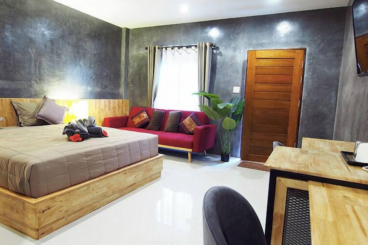 A modern bedroom with a large bed, a red sofa, a wooden desk, and a large window with curtains.