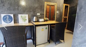 A compact room with a kitchenette, two wicker chairs, a small fridge, a wooden table, and artwork on the wall. - Paradise Land Resort (Pattaya)