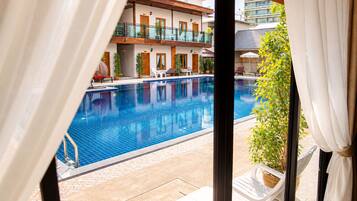 Zona d'una piscina d'hotel amb vista clara a la piscina, gandules i un edifici amb balcons.