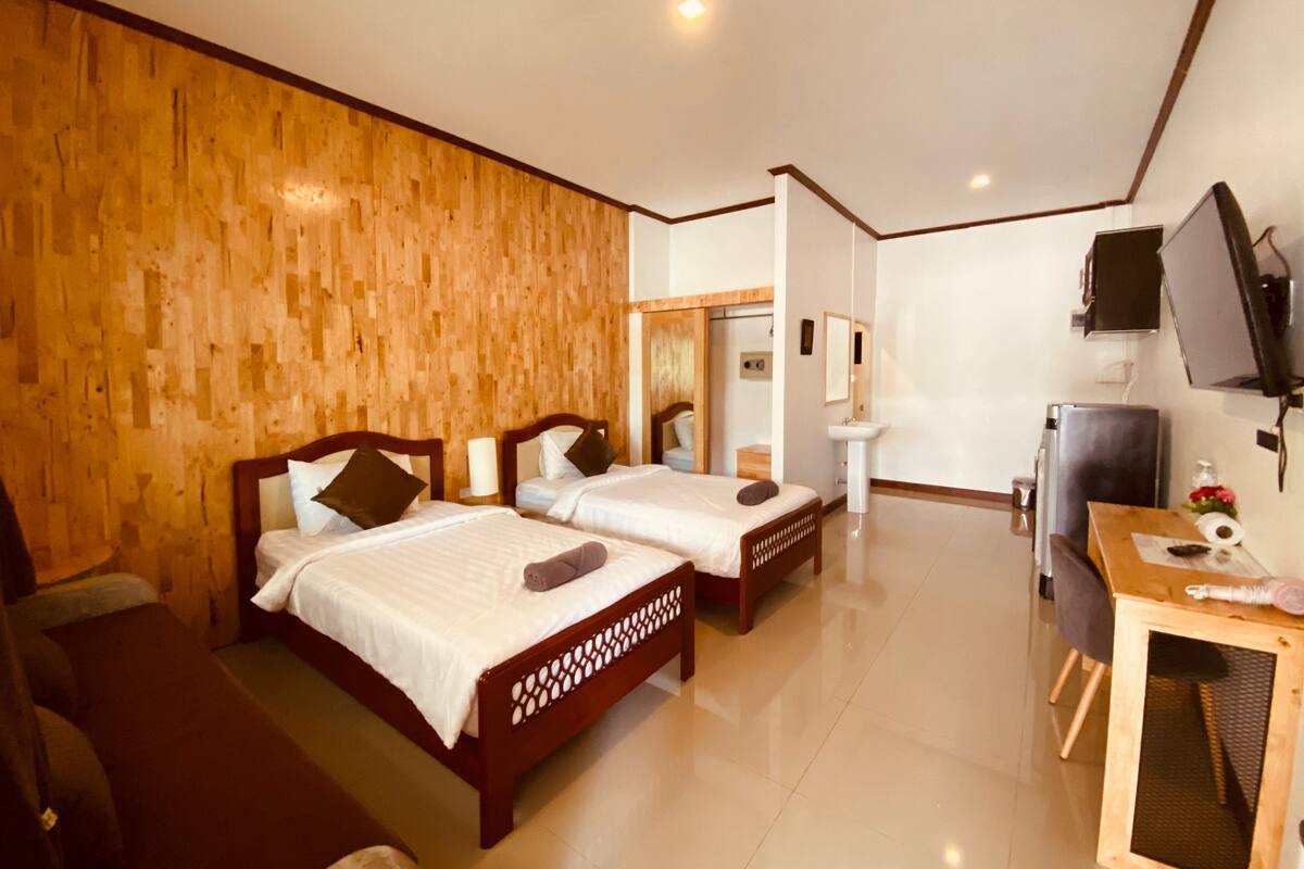 A hotel room with two wooden beds, a desk with a computer, a TV, and a mirror.