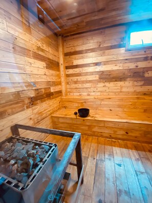 L’intérieur d’un chalet en bois, avec un banc en métal et un bol noir posé sur une étagère en bois.