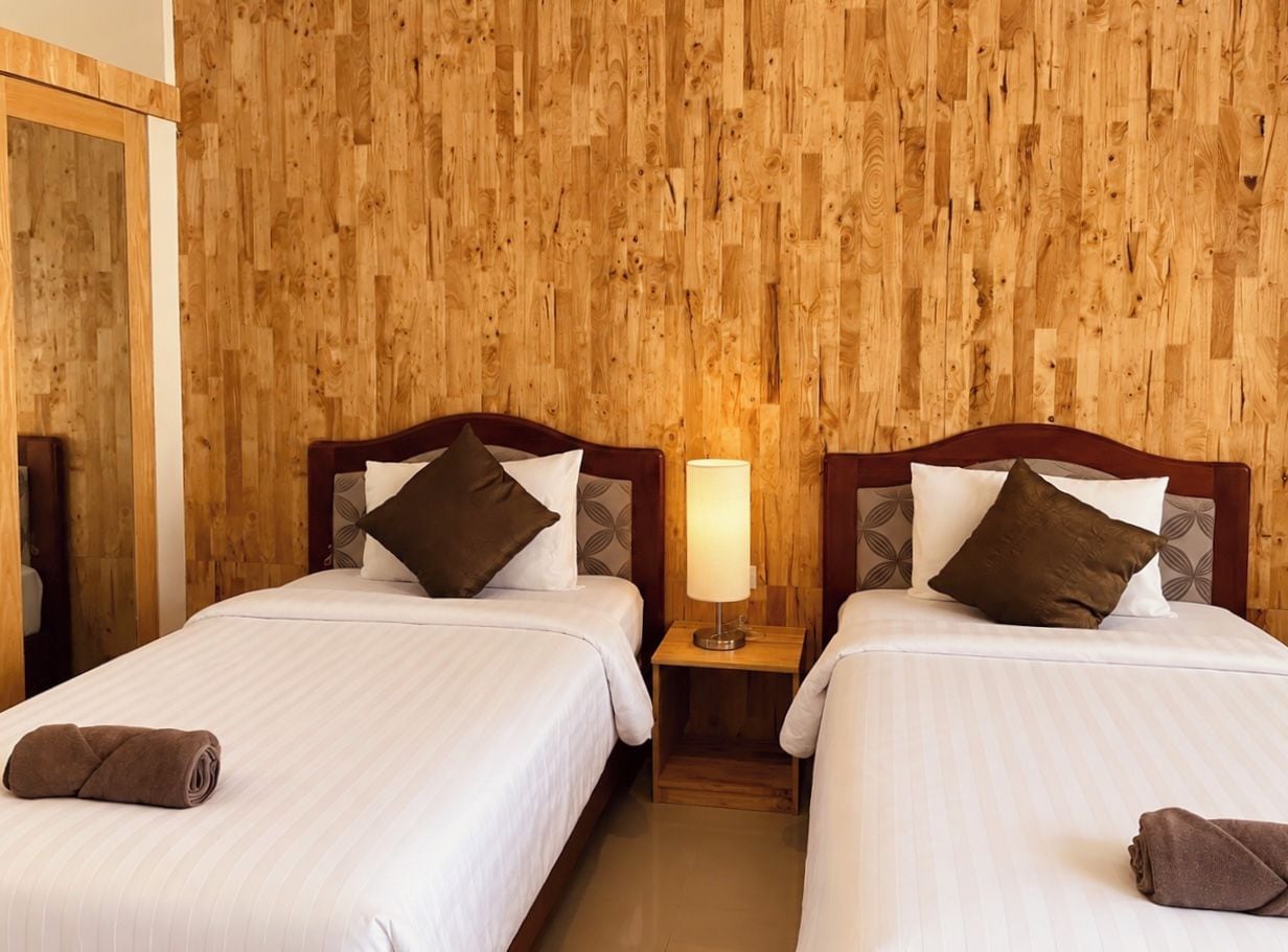 A hotel room with two beds, wooden panel walls, a nightstand with a lamp, and a mirror.
