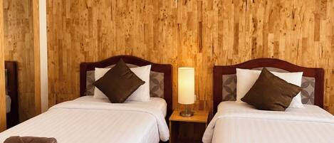 A hotel room with two beds, wooden panel walls, a nightstand with a lamp, and a mirror.