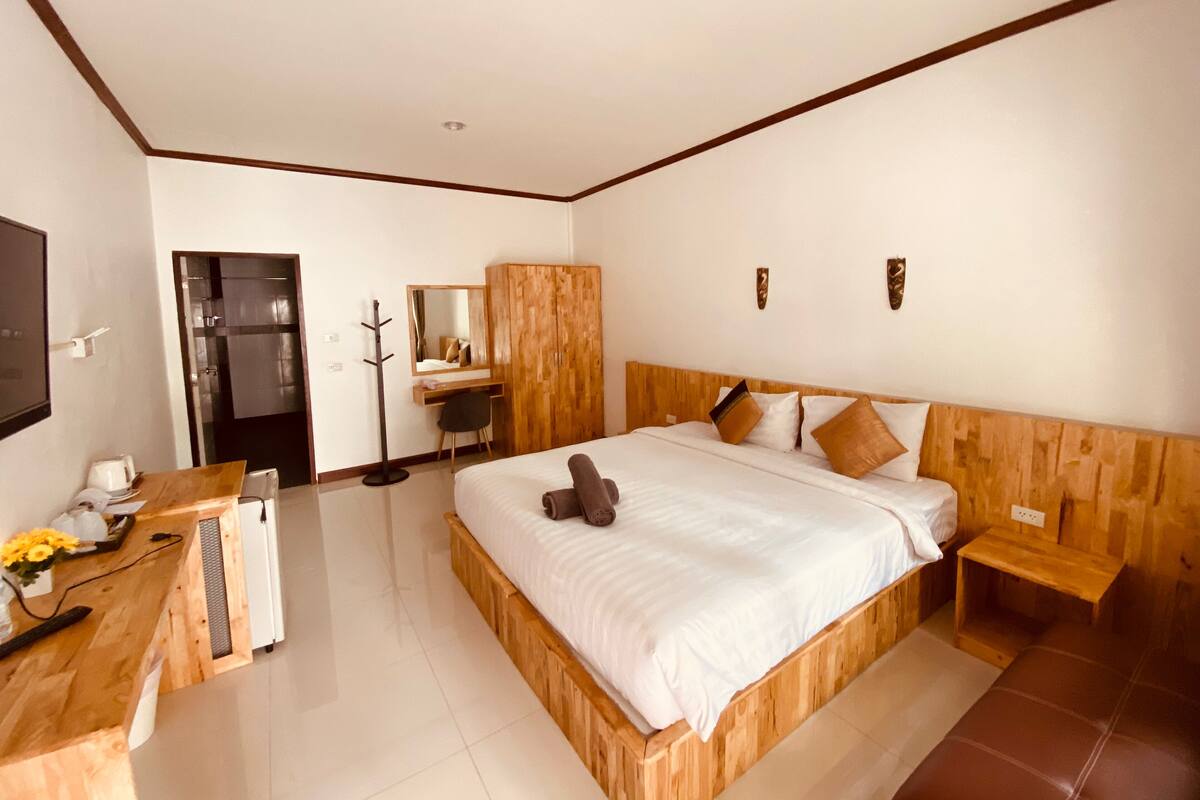 A bedroom with a wooden bed, a desk, a chair, a mirror, and a wardrobe.