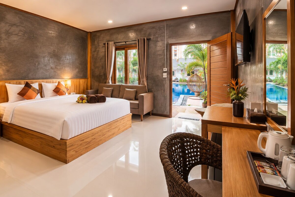 A modern hotel room with a large bed, a desk with a chair, a television, and a view of a swimming pool.