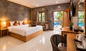 A modern hotel room with a large bed, a desk with a chair, a television, and a view of a swimming pool. - Paradise Land Resort (Pattaya)