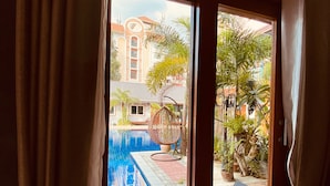 Vista desde una habitación a través de una ventana con cortinas, que da a una piscina y un edificio con techo de tejas.