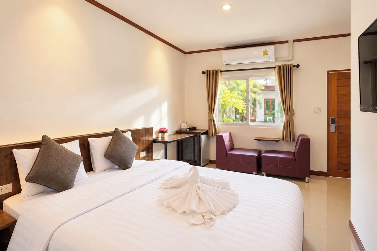 A hotel room with a large bed, a desk, a chair, an air conditioning unit, and a window with curtains.