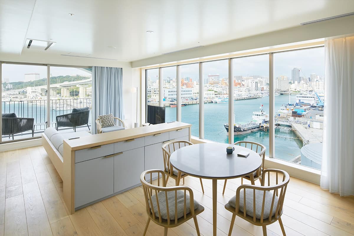 A modern hotel room with a large window overlooking a marina and cityscape.
