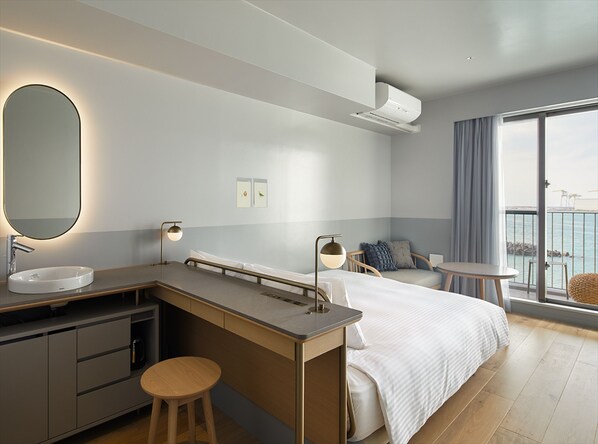 Una habitación de hotel moderna con una cama grande, un escritorio con lavamanos y un balcón con vistas al mar.