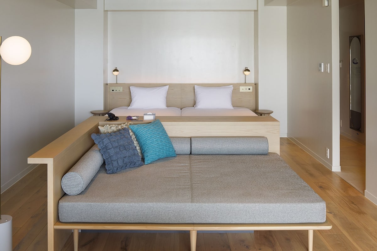 A modern bed with a wooden frame, a headboard with integrated lighting, and a bedside table with a lamp.