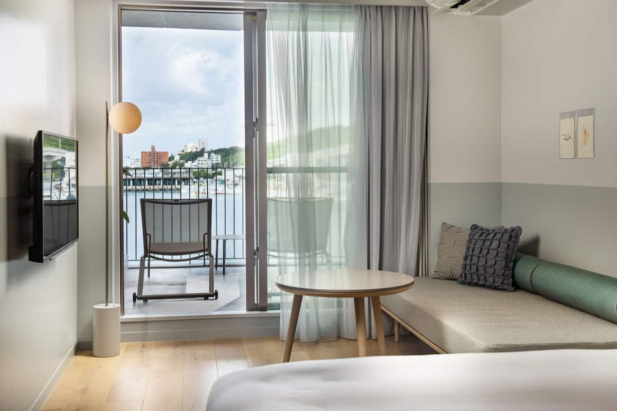 A hotel room with a balcony, a bed, a sofa, a table, and a TV.