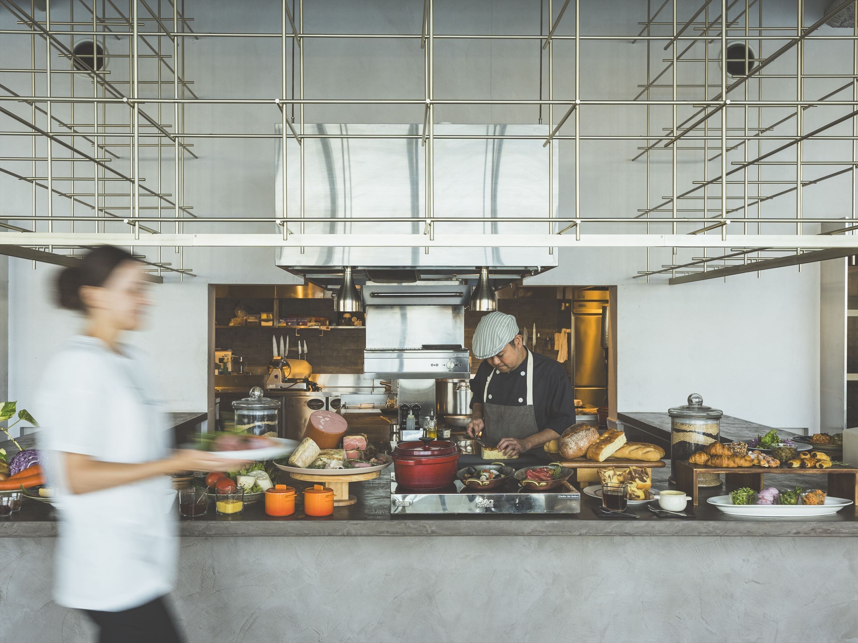 A modern kitchen with stainless steel appliances, a chef preparing food, and a buffet area with various dishes.