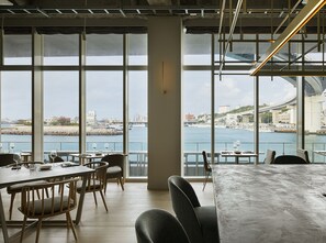 Un comedor moderno con amplios ventanales con vista a un paisaje urbano frente al agua.