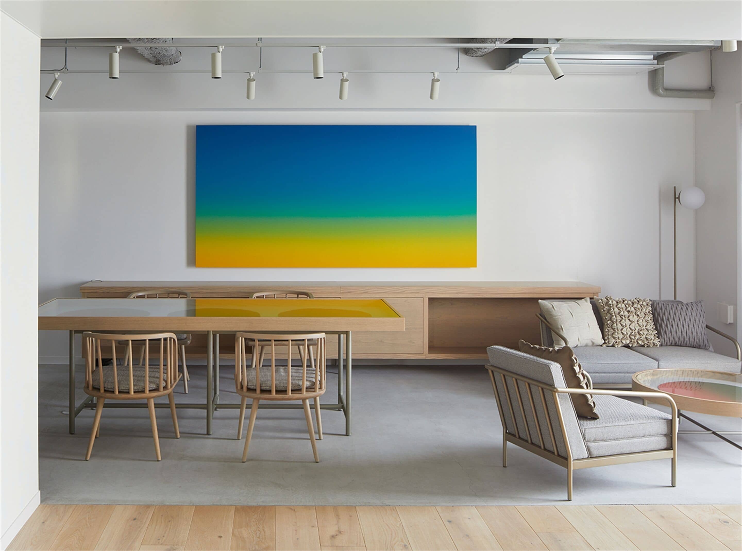 A modern living room with a dining area, featuring a large wall-mounted artwork, wooden furniture, and a minimalist design.