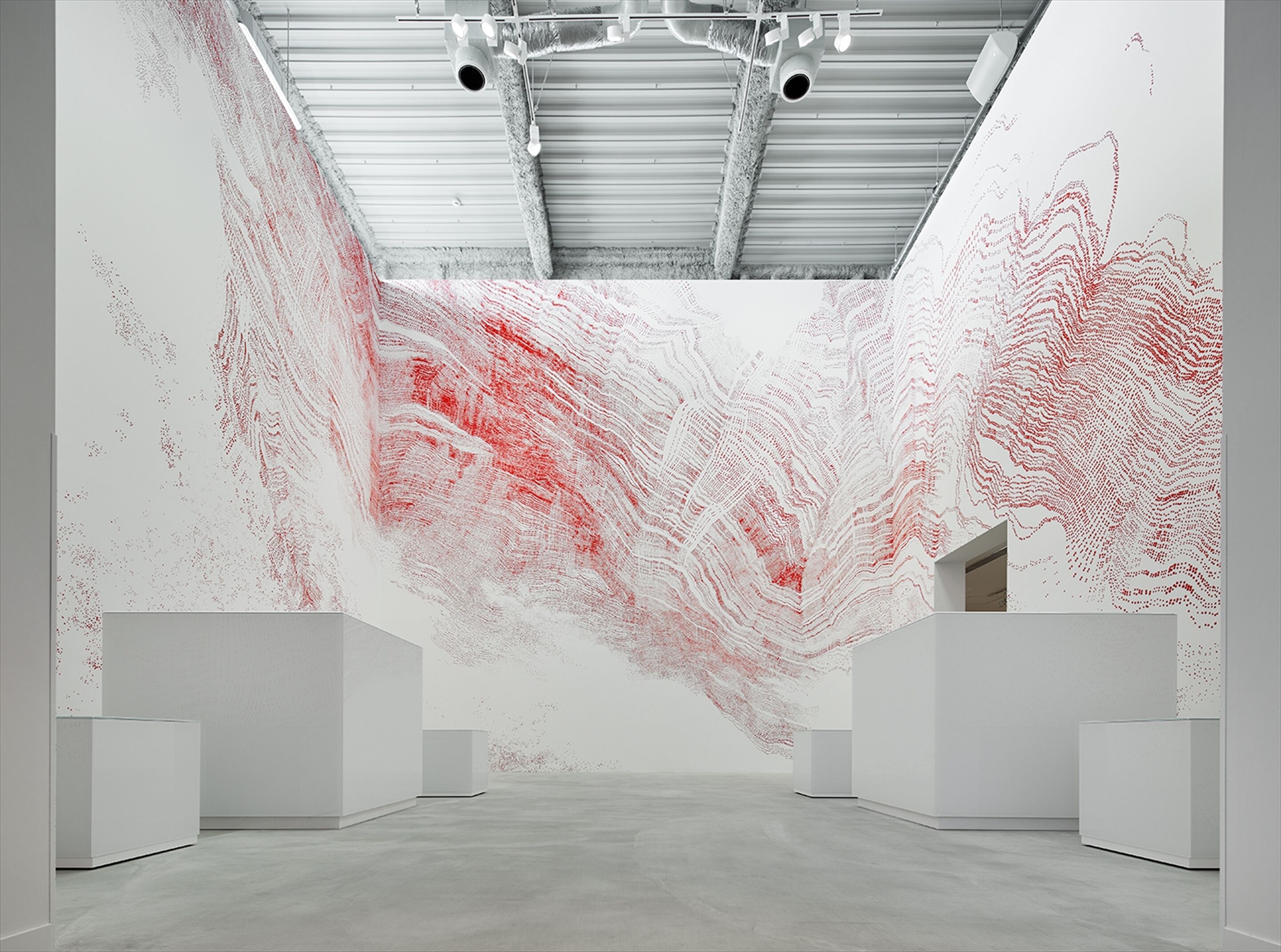 Een kunstgalerie met witte muren en een betonnen vloer, met abstracte schilderijen in rood en wit.