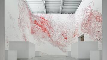 Een kunstgalerie met witte muren en een betonnen vloer, met abstracte schilderijen in rood en wit.