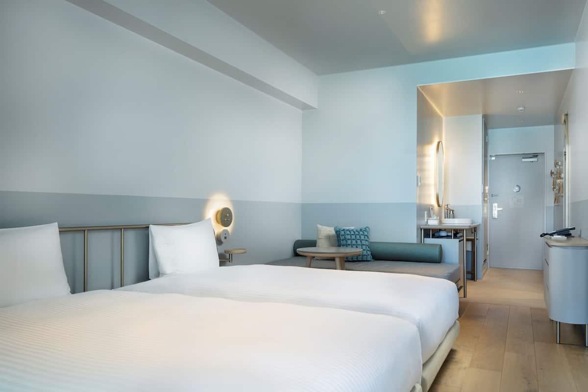 A modern hotel room with a large bed, a small seating area, a desk, and a bathroom.