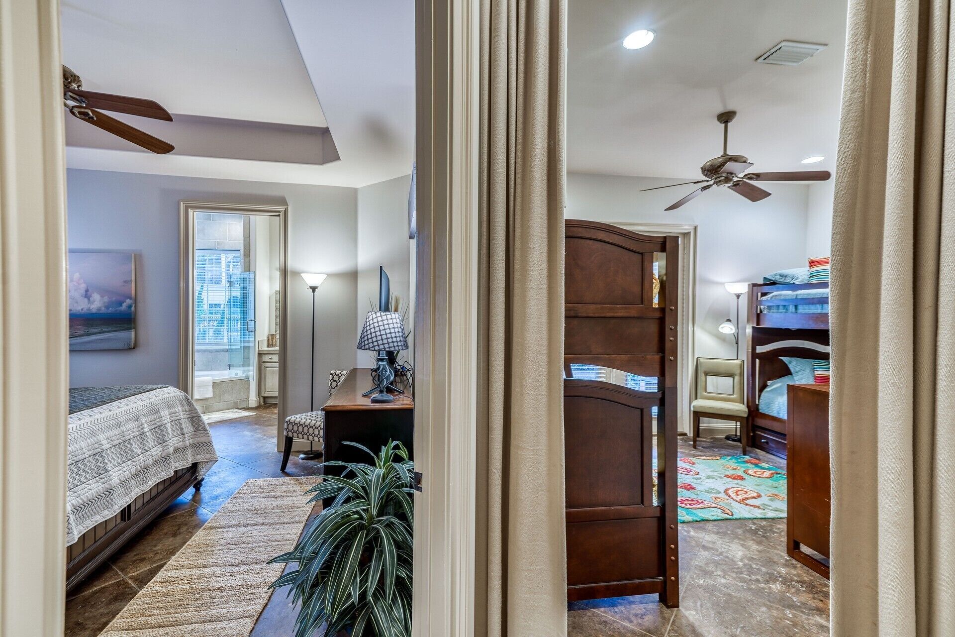 A bedroom with a bed, a desk, a chair, a ceiling fan, and a window with a view.