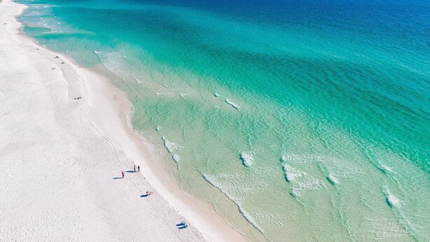 Eine Luftaufnahme eines Strandes mit klarem türkisblauem Wasser und einem Sandufer.