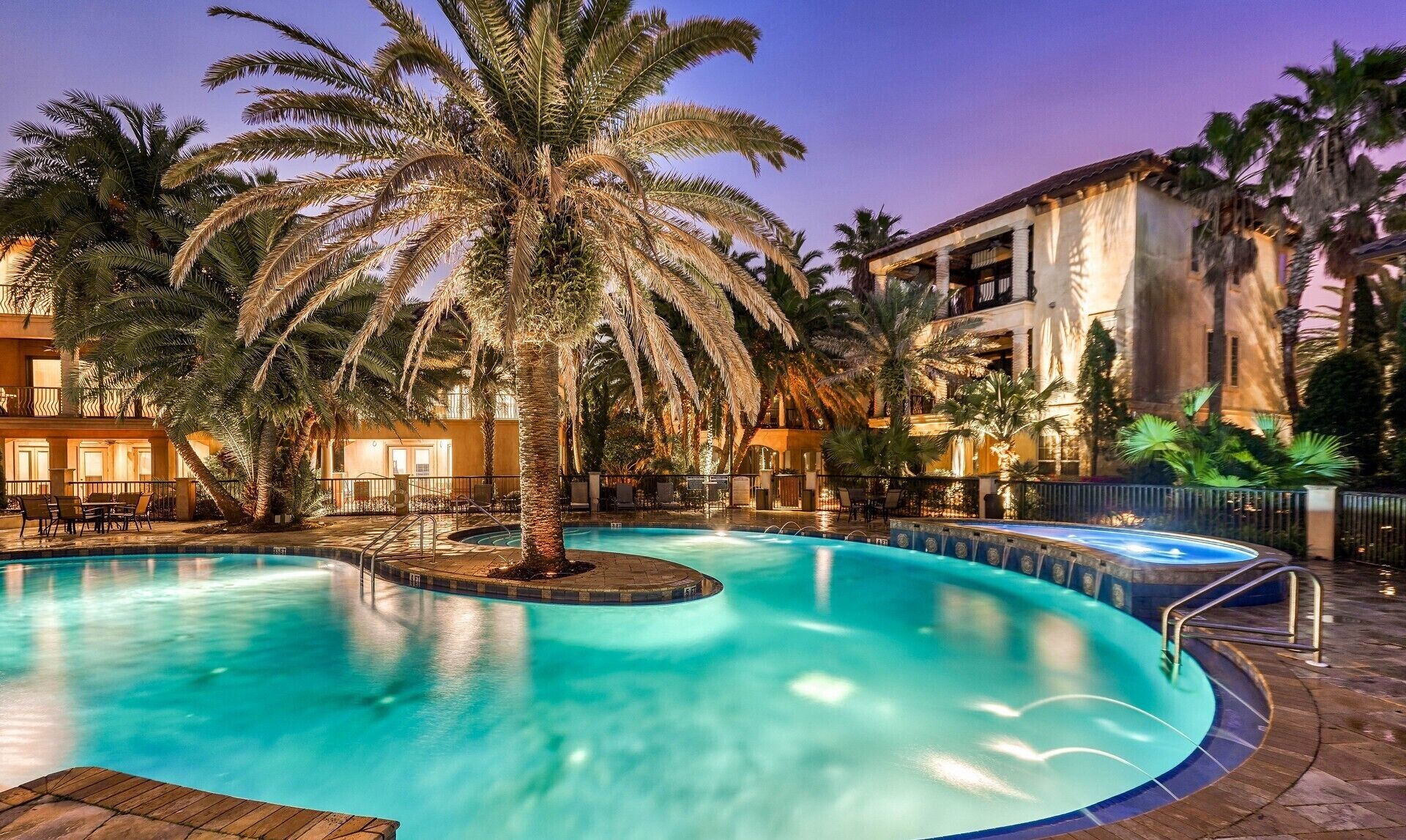A swimming pool with a palm tree in the center, surrounded by a poolside area with lounge chairs and a building in the background.