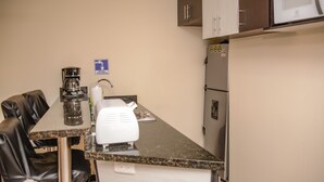 A kitchenette with a coffee maker, microwave, refrigerator, and a sign indicating water availability.