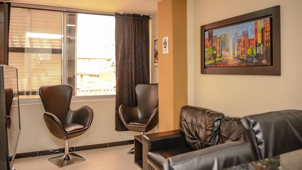 A modern living room with a black leather sofa, two black leather chairs, a painting on the wall, and a window with curtains.