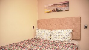 A bedroom with a large bed, patterned bedding, a headboard, and a painting on the wall.