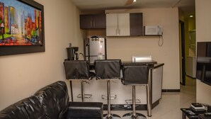A compact living space with a kitchenette, a dining area with bar stools, a black leather sofa, and a ceiling fan.