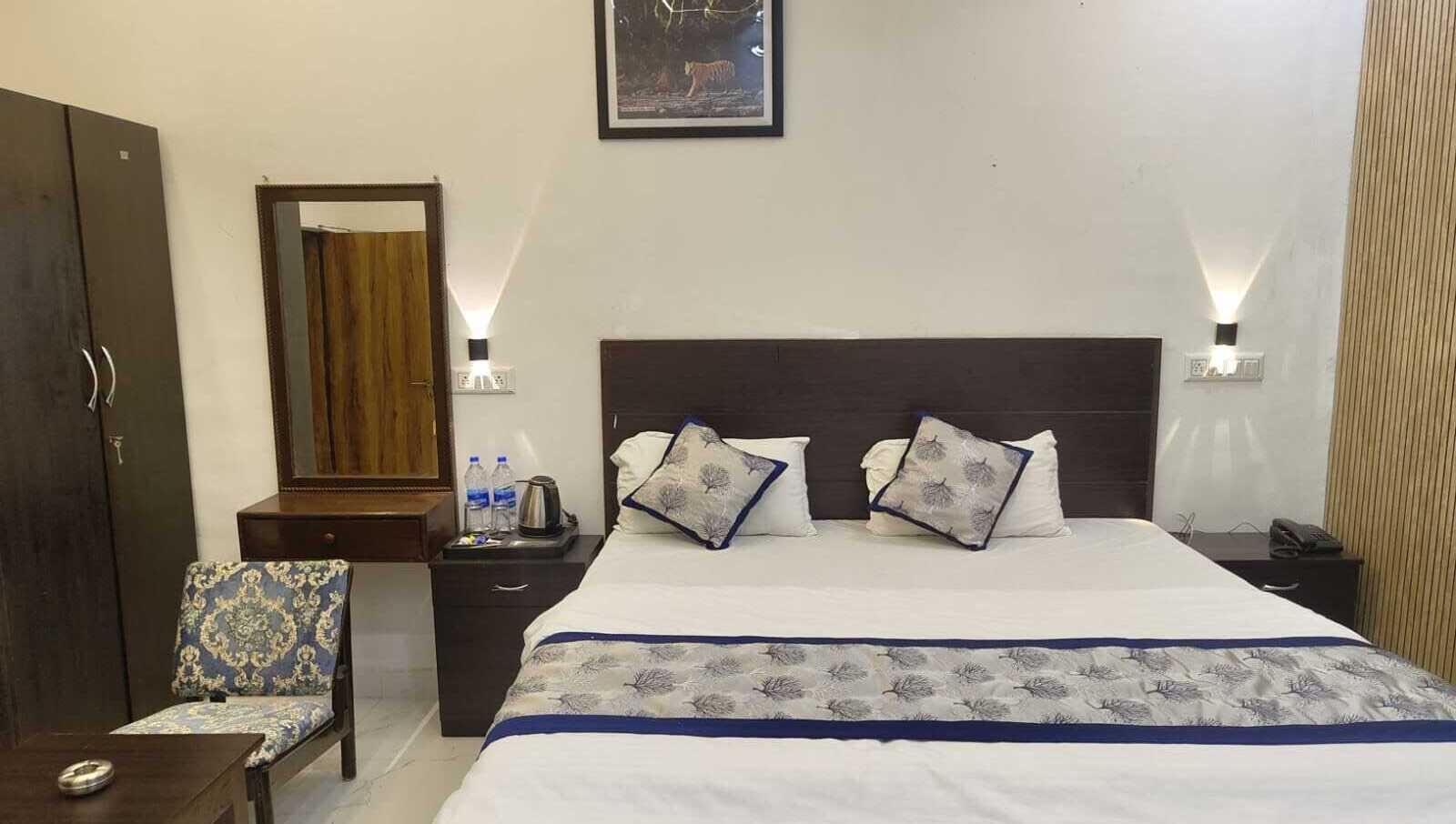 A hotel room with a large bed, a chair, a nightstand with a lamp, a wardrobe, and a mirror.