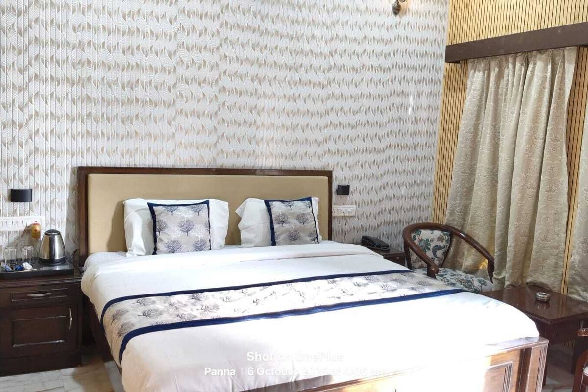 Quarto de hotel com cama, mesas de cabeceira, uma cadeira e papel de parede estampado.