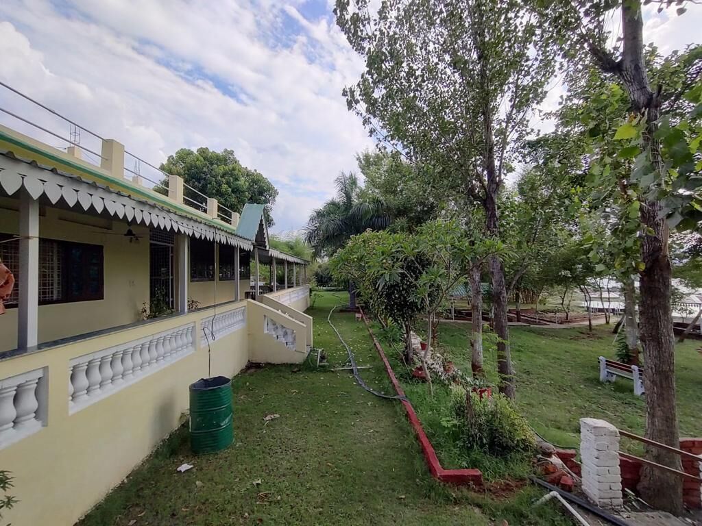Un edificio con balcón, un barril verde y un jardín con árboles y un borde rojo.