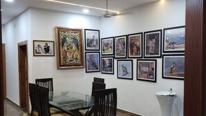 Un comedor con una mesa de vidrio rodeada de sillas, un lavamanos pedestal blanco y una pared decorada con obras de arte enmarcadas.