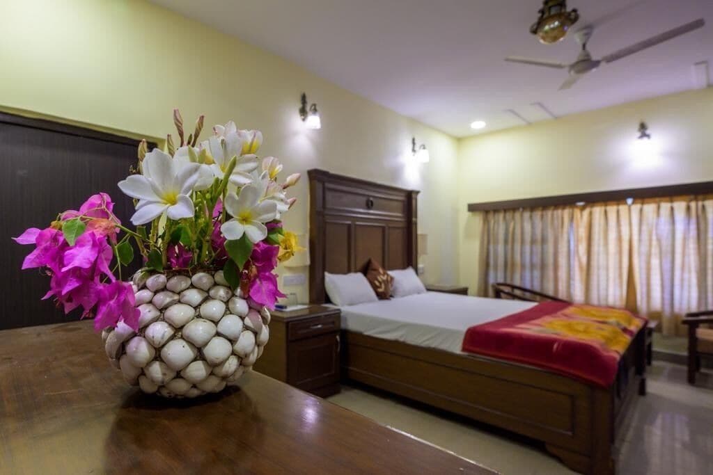 A hotel room with a bed, bedside table, and a vase of flowers.