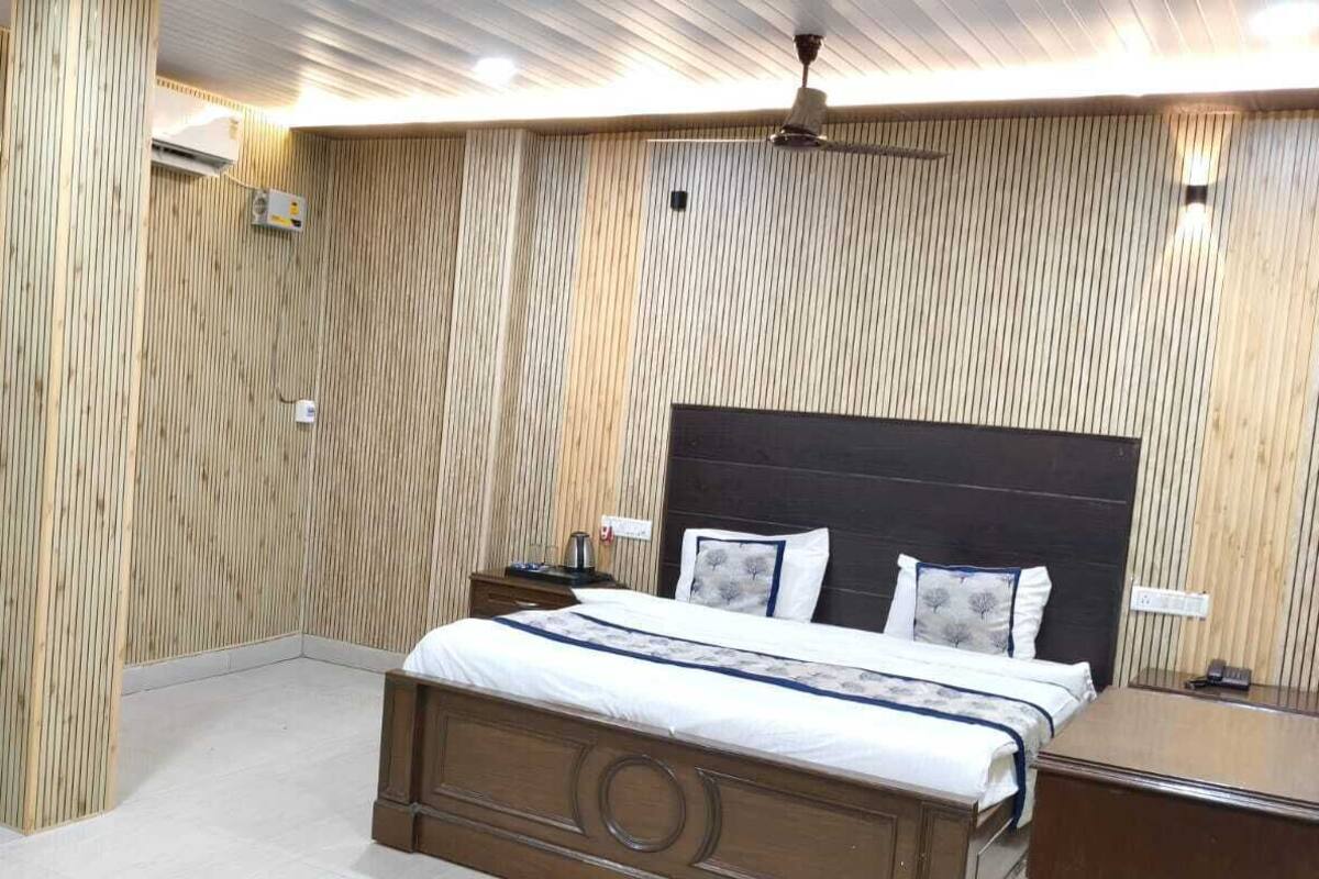 Quarto com parede de painel de madeira, cama com cabeceira escura, poltrona verde, mesa de cabeceira e criado-mudo.