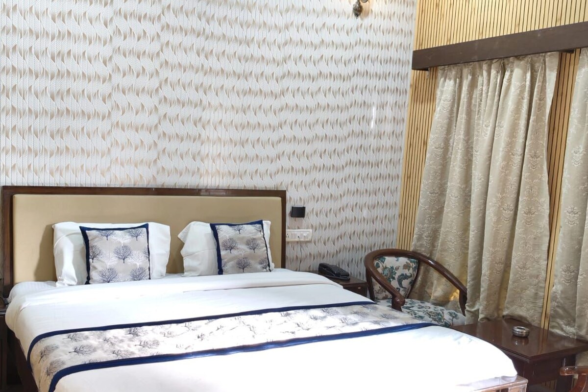 Una habitación de hotel con cama, mesitas de noche, una silla y papel tapiz estampado.