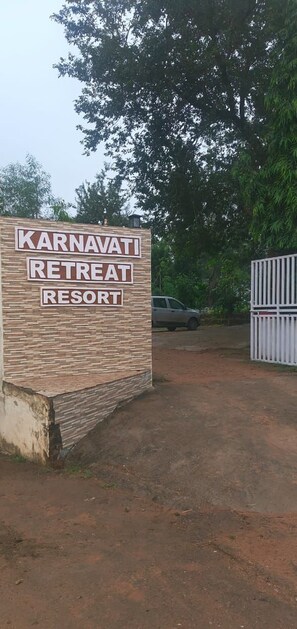 Señal para Karnavati Retreat Resort con entrada vigilada y un coche estacionado.