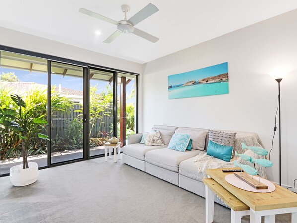 A modern living room with a white sofa, a wooden coffee table, and a painting of a beach scene. - Adelong (Buddina)