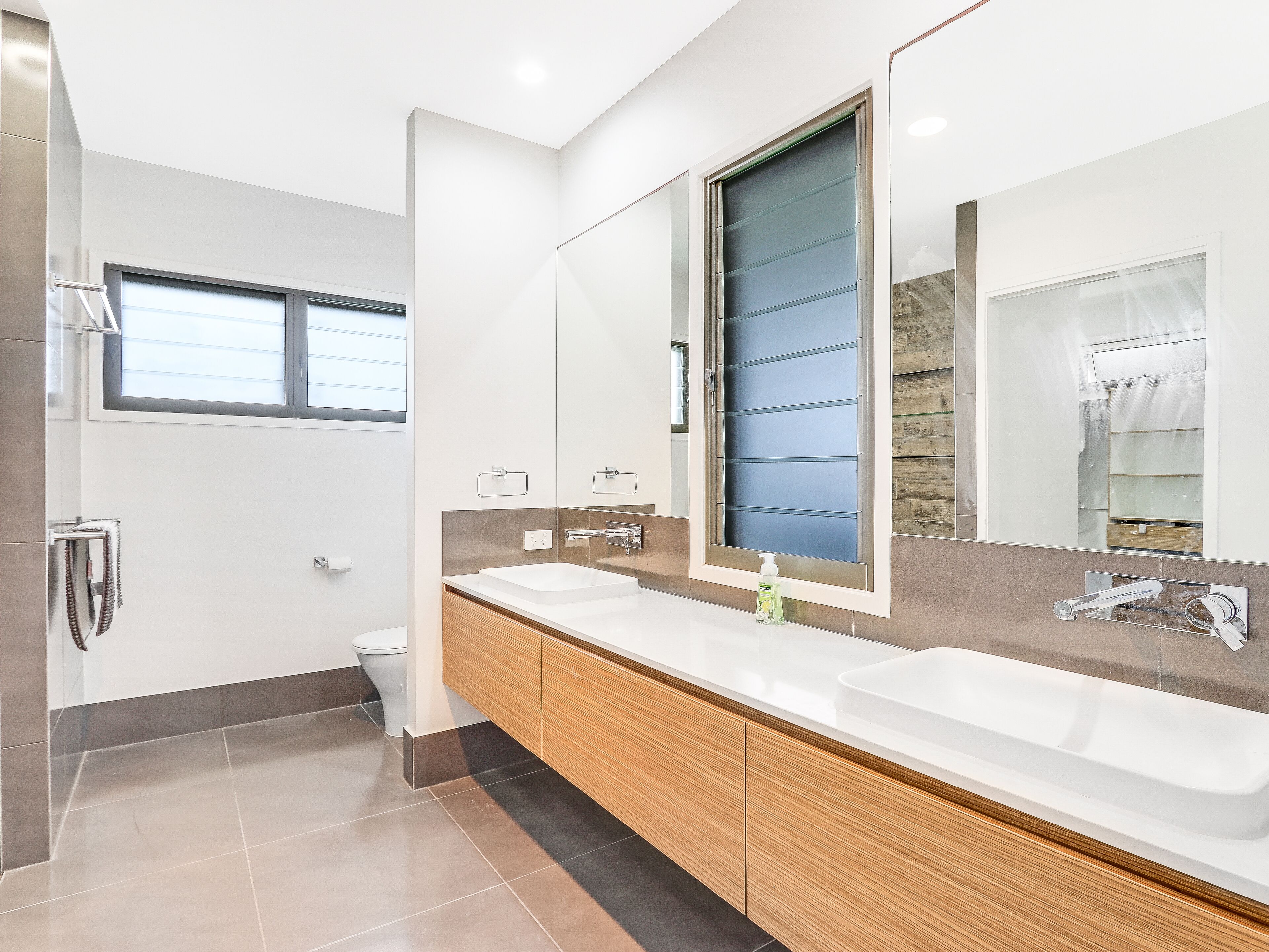 A modern bathroom with a large mirror, two sinks, and a shower.