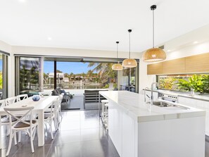 A modern kitchen with a large island, white cabinetry, and a view of a pool and outdoor area. - Adelong (Buddina)