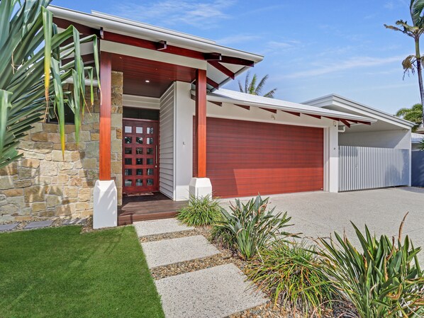 A modern house with a stone facade, a red garage door, and a well-maintained lawn. - Adelong (Buddina)