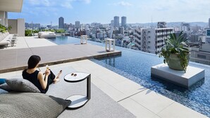 Piscina infinita en la azotea con vista a la ciudad, un área de descanso y una planta en maceta.