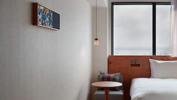 Habitació d'hotel amb un llit, una taula rodona petita amb una cadira, un quadre penjat a la paret, una finestra amb vistes i una làmpada penjant.