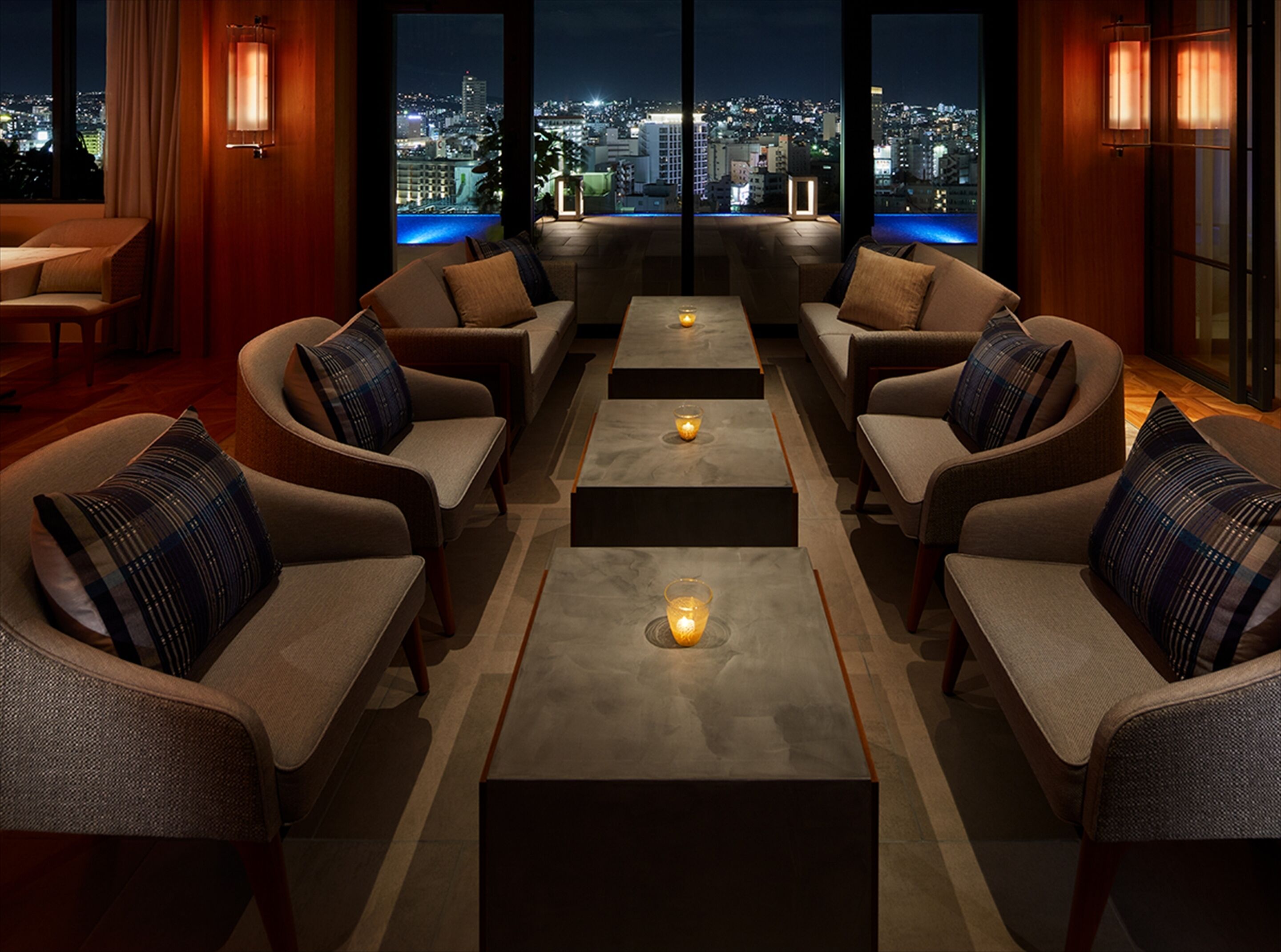A modern lounge area with sofas and tables, large windows offering a city view at night.