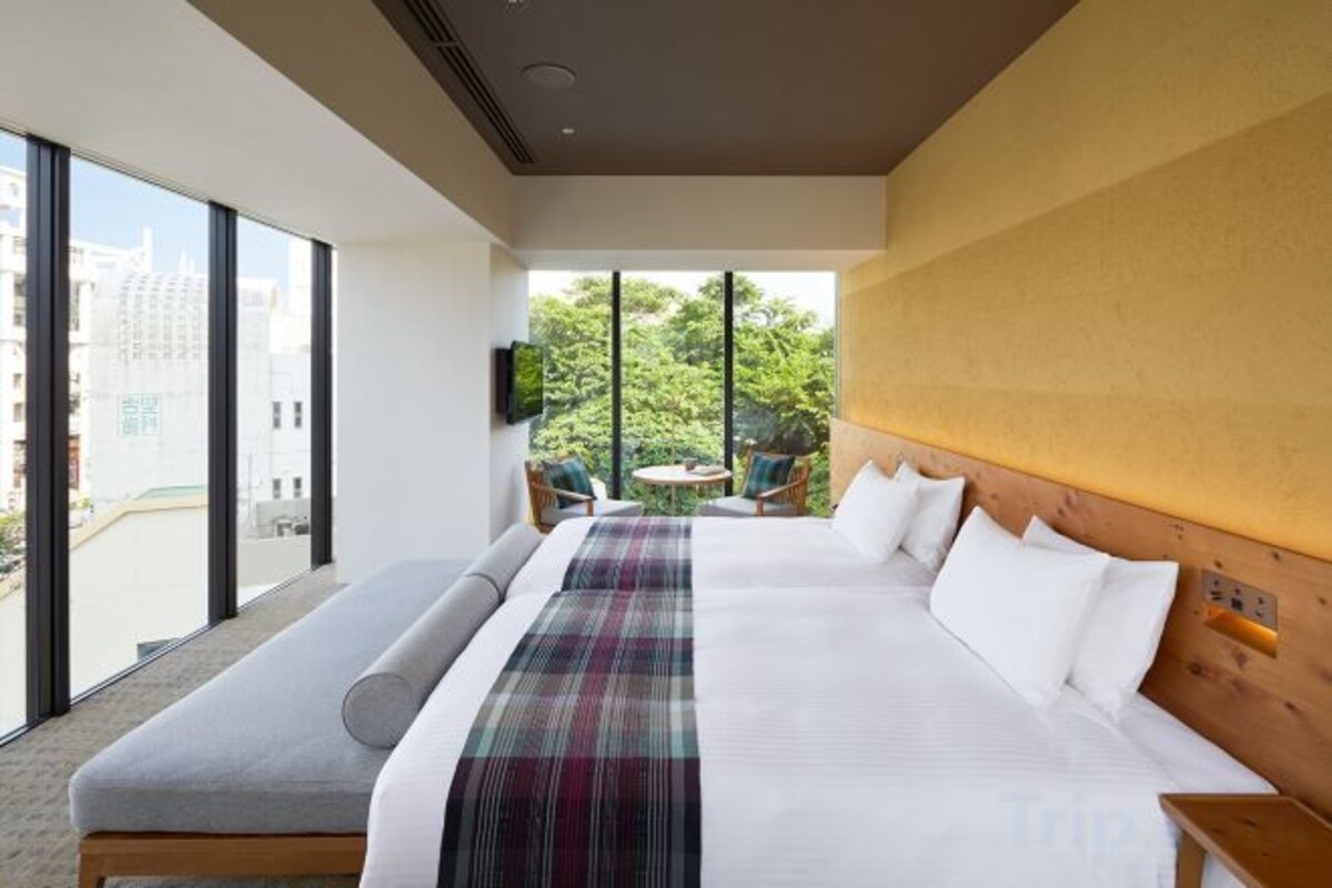 A hotel room with a large bed, a bench, a small table, and a view of the outdoors.
