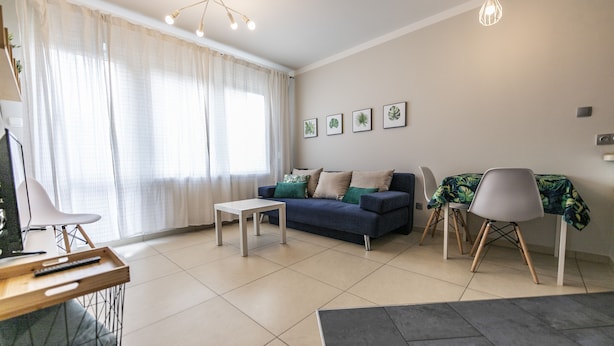 A modern living room with a sofa, a coffee table, and a dining area with chairs. - Victus Apartamenty - Avocado (Sopot)