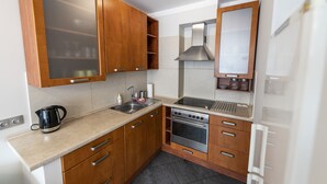 A compact kitchen with wooden cabinets, a stainless steel stove, and a built-in oven. - Victus Apartamenty - Avocado (Sopot)