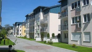 A row of modern apartment buildings with balconies, a paved driveway, and small landscaped areas. - Victus Apartamenty - Avocado (Sopot)